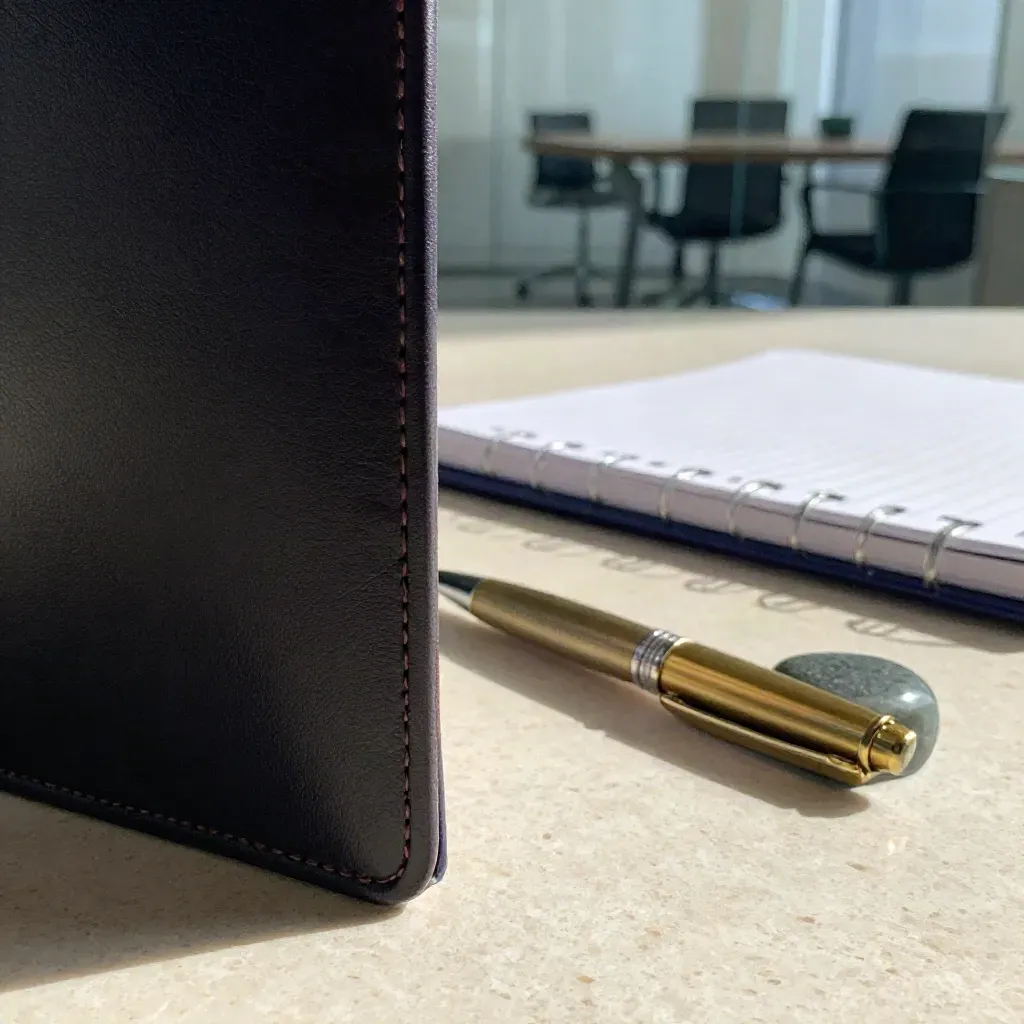 Macro still life of a leather strategy folio, brass pen, stone weight and tabbed notebook on travertine.
